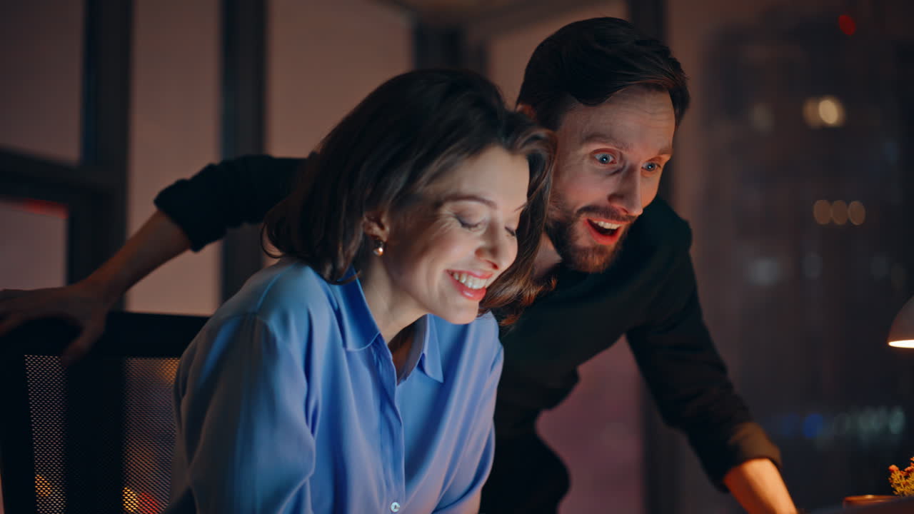 Surprised colleagues rejoicing achievement looking laptop at dark office closeup