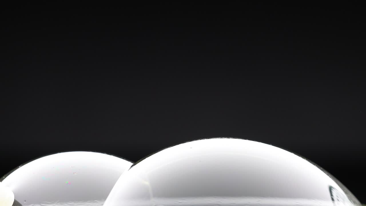 A wand interacts with soap bubbles, creating reflections and colors against a dark background in a minimalist setting