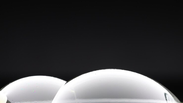A wand interacts with soap bubbles, creating reflections and colors against a dark background in a minimalist setting