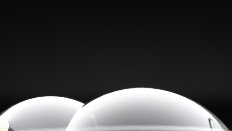 a wand interacts with soap bubbles, creating reflections and colors against a dark background in a minimalist setting