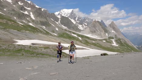 couple walks through green meadows and snowy peaks during a scenic mont blanc hike in switzerland, front view with ice on mountains