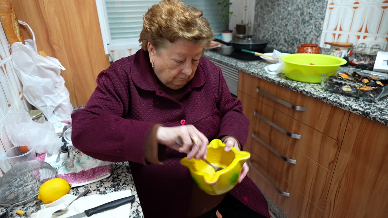 la abuela mezclando ingredientes en un cuenco para la salsa, sentada en la cocina