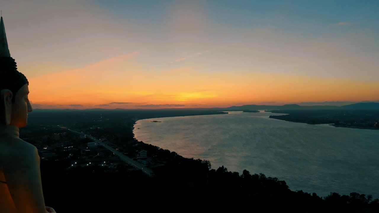 imágenes de 4k de una impresionante puesta de sol sobre el poderoso río mekong en laos, observada pacíficamente por una gran estatua de buda