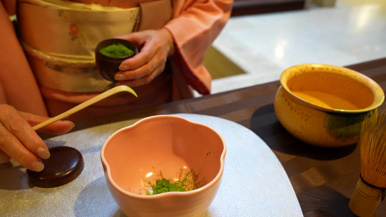 Donna che esegue una tradizionale cerimonia del tè giapponese, aggiungendo polvere di matcha in una ciotola con un cucchiaio.