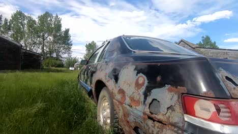 Old rusty car sitting in a grassy field on a sunny day during the summer with a blue sky and clouds overhead.