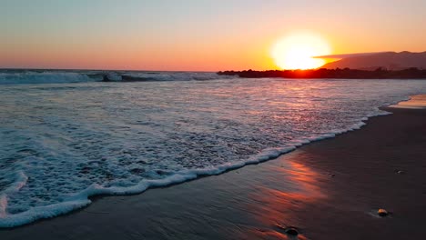 Tiro-De-Cardán-Muy-Bajo-De-La-Playa-Al-Atardecer-Con-Olas-Rompiendo-En-La-Playa-Estatal-De-San-Buenaventura-En-Ventura,-California,-Estados-Unidos