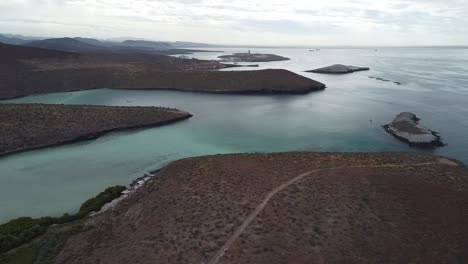 Playa-balandra-with-clear-turquoise-waters-and-surrounding-desert-landscape-at-dusk,-aerial-view