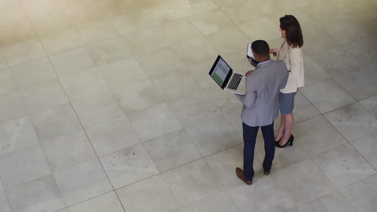 Diversos empresarios y empresarias hablando y usando un portátil en el vestíbulo de una oficina moderna