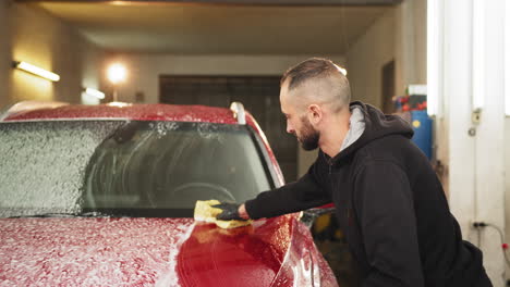 man washing a red car in a garage