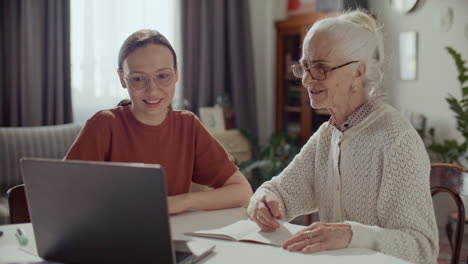 elderly woman learning how to use the internet on laptop with help of caregiver
