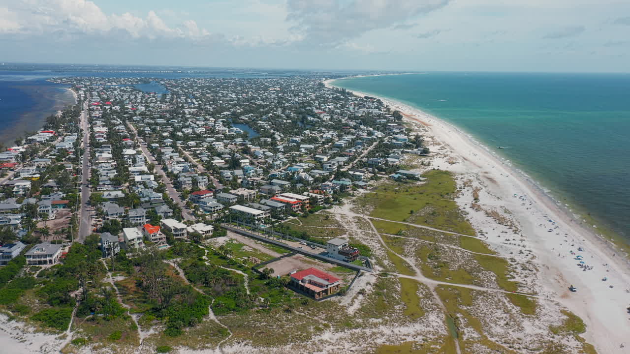 A sweeping view of Anna Maria Island reveals a crescent-shaped shoreline with soft sandy beaches, turquoise waters, and a coastal town nestled along the edge of the sea