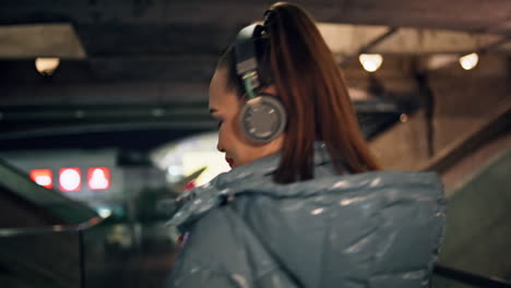 Mujer-Caminando-En-El-Metro-Oscuro-Con-Auriculares-Escuchando-Música-De-Cerca-Vista-Posterior