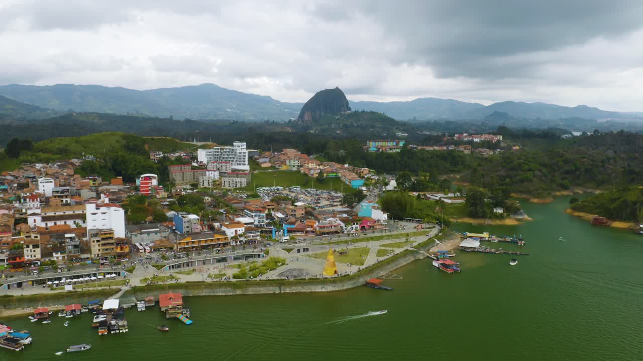 el vuelo aéreo hacia atrás revela el colorido pueblo de guatapé con la piedra del peñol al fondo