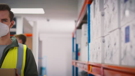 portrait of male worker wearing ppe face mask holding box inside warehouse