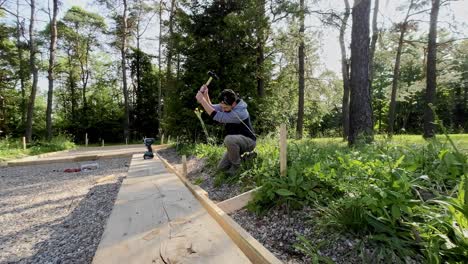 carpenter hitting a wooden stake into the ground while installing forms for a concrete pad in a forest.