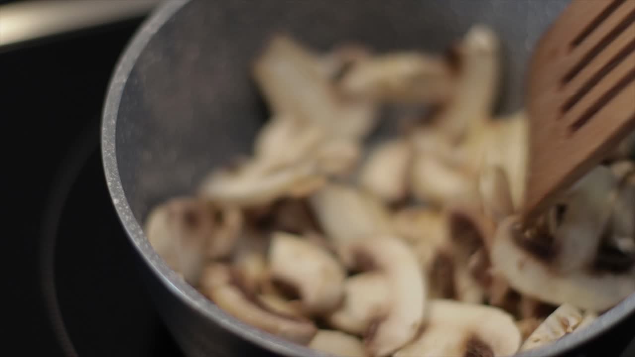 작은 프라이팬에 버섯을 요리하고 나무 숟가락으로 섞는다.