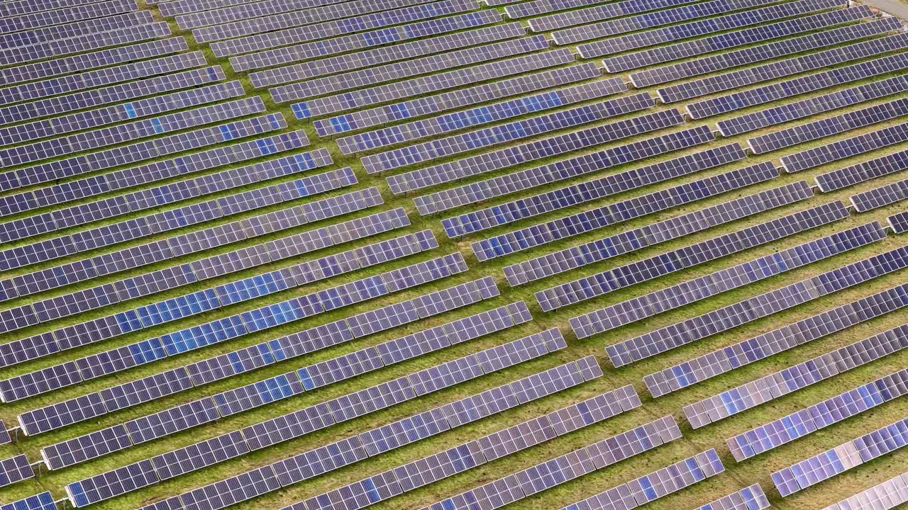 Drone camera smoothly pans above rows of solar panels under natural daylight, emphasizing renewable energy