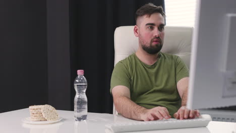 Man-Drinking-Water-From-Plastic-Bottle-While-Using-Desktop-Computer-At-Office