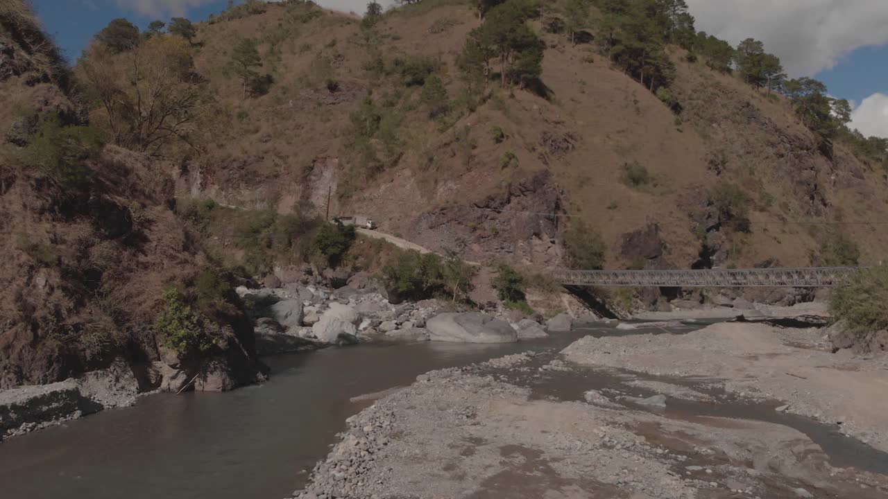 río rocoso que serpentea a través de las montañas en el valle del cañón agua que fluye acercándose rocas grises árboles verdes cielo azul lento aéreo suave avanzando puente en la distancia conectando