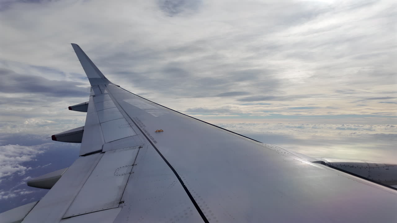 Aircraft wing gliding above layered clouds viewed from the window seat