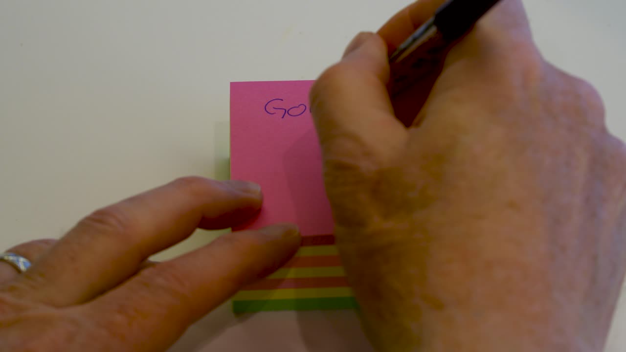 Hand seen writing, "Going to Lunch" on a pink, sticky, post it pad and then tearing off the top sheet - isolated close up