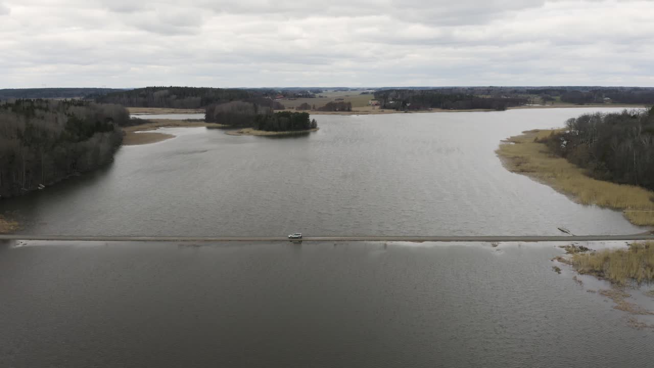 Aerial of car driving over thin dirt road through lake