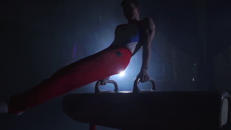 male gymnast athlete performs handstand and rotation on pommel horse on dark background and smoke in slow motion