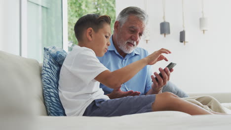 Hispanic-Grandson-Showing-Grandfather-How-To-Use-Mobile-Phone-At-Home