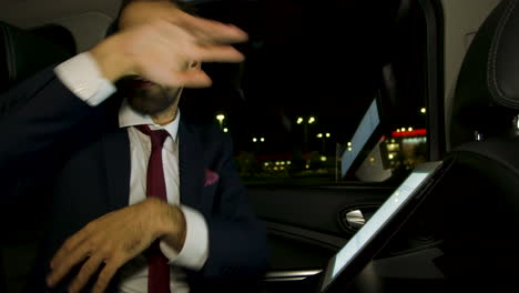 Serious-businessman-working-on-tablet-at-night-in-the-back-seat-of-his-limousine-with-personal-driver