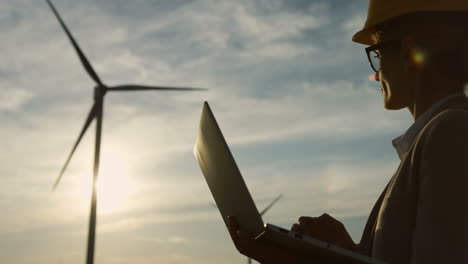 Silhouette-Einer-Kaukasischen-Ingenieurin,-Die-Einen-Helm-Trägt-Und-Einen-Laptop-An-Einer-Windstation-Für-Erneuerbare-Energien-Verwendet