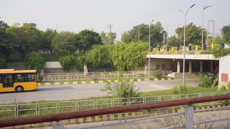 yellow bus driving under an overpass on a sunny day