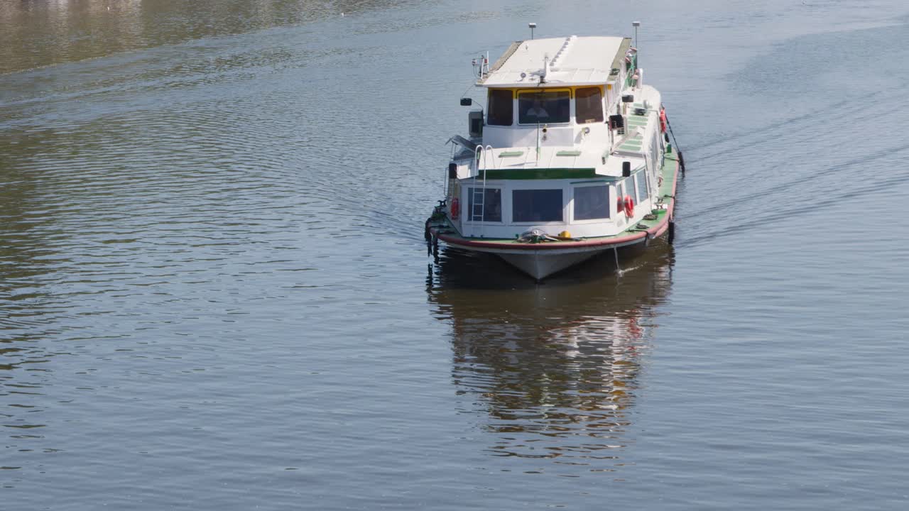 Passenger boat steadily approaches on calm Vltava River, daylight, steady camera, summer atmosphere