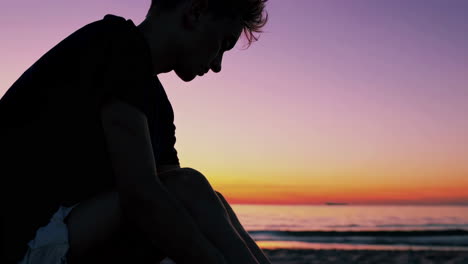 man sitting alone on the beach at sunset