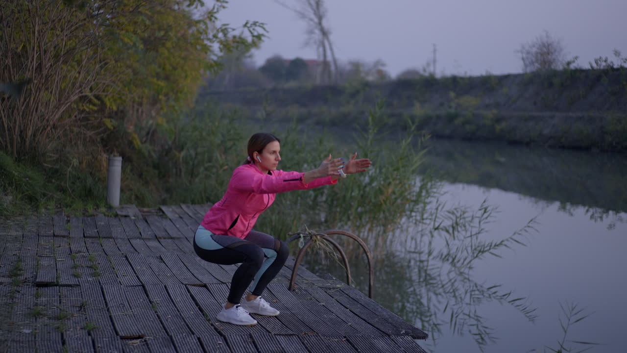 Woman exercising and performing squats on a wooden deck by the river