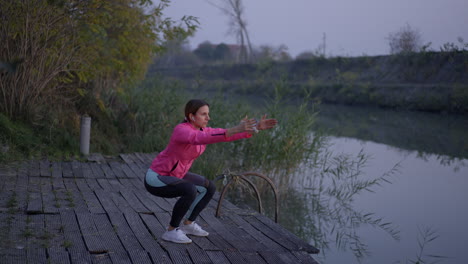 woman exercising and performing squats on a wooden deck by the river