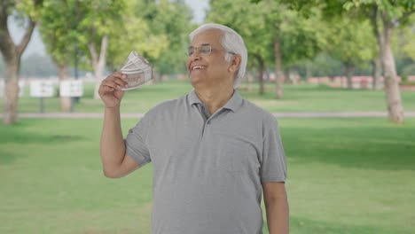 happy indian old man using money as fan in park