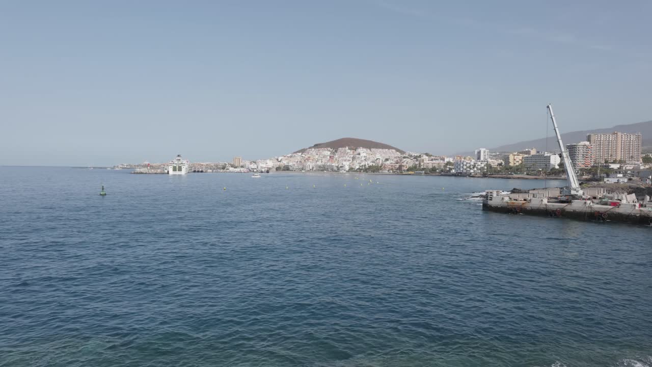 A port and apartments by the sea on a hill on a sunny day in Los Cristianos, Tenerife, Canary Islands, Spain.