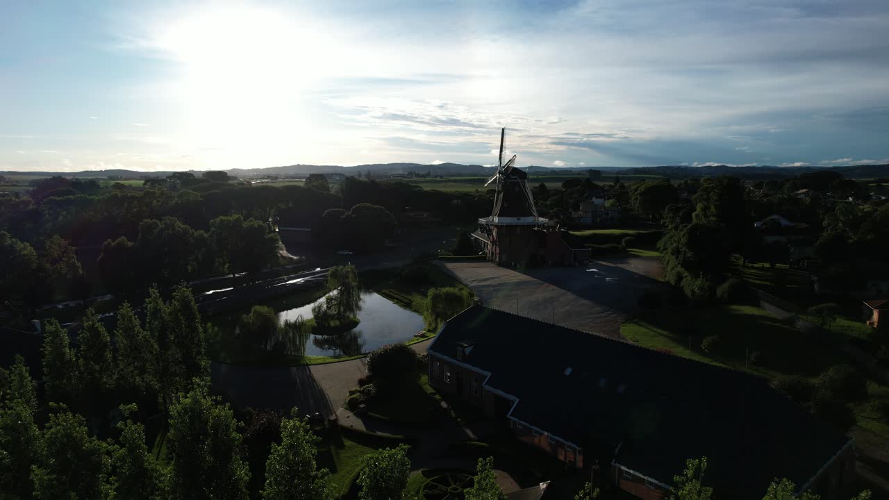 Side tracking shot with drone in the backlight of the sunset showing a beautiful lake and a replica of a Dutch windmill, magical and soft light