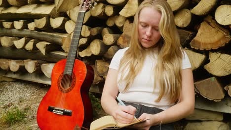 young female guitarist songwriter composes lyrics rustic log scene