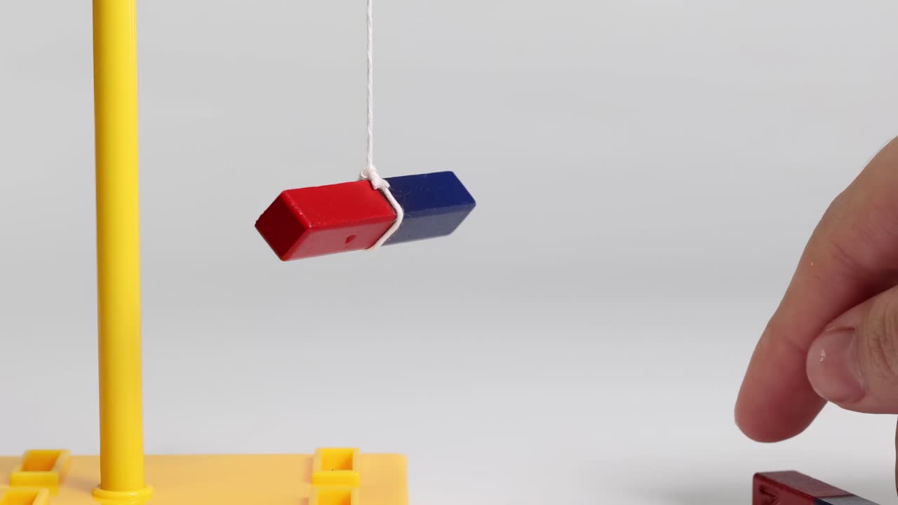 A suspended red and blue magnet interacts with a handheld magnet, demonstrating magnetic forces.