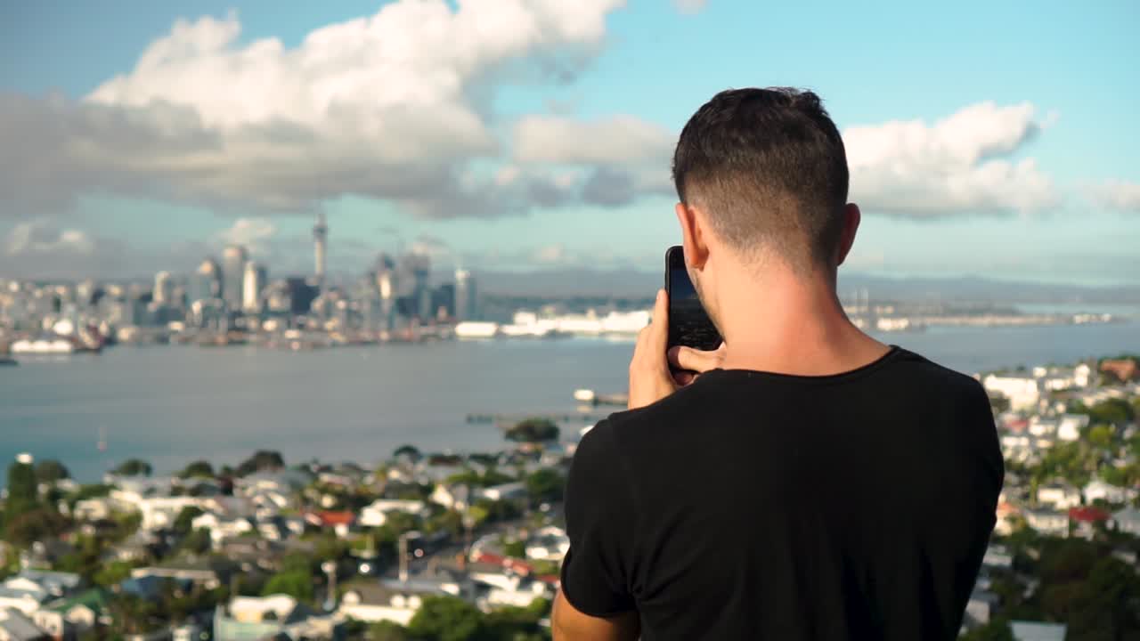 SLOWMO - Young caucasian man taking photo with phone of Auckland skyline from Devonport, New Zealand