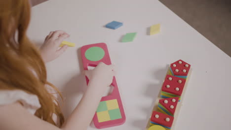 vista superior de una niña pelirroja jugando con un clasificador de formas en una escuela montessori