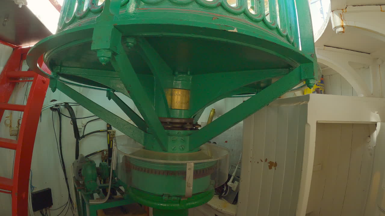 낮 동안 천천히 회전하는 램프 아래에서 움직이는 등대 렌즈 메커니즘과 모터의 정적 실내 샷