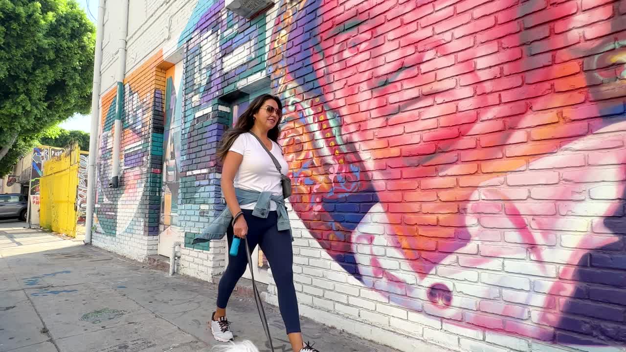 Donna latina che porta a spasso il suo cane maltese nel Distretto Artistico di Los Angeles.
