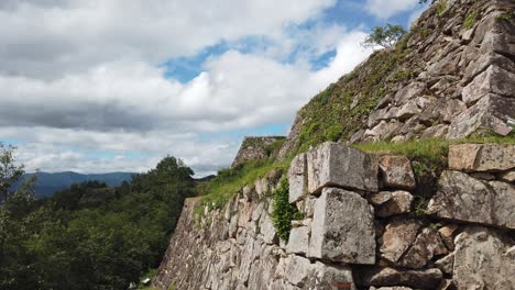 Outer-brick-wall-of-Takeda-castle-ruins-in-Asago-Hyojo-Japan,-pan-across-weathered-rocks-on-cloudy-day