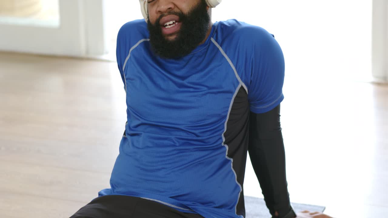 African American man in sportswear pushing up after set on mat at home, putting on headphones