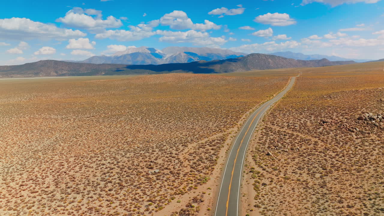 Highway crossing the dry landscape. Itinerary though the deserted land to Nevada, USA. Mountains at backdrop.