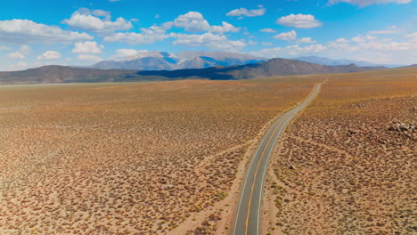 Highway crossing the dry landscape. Itinerary though the deserted land to Nevada, USA. Mountains at backdrop.