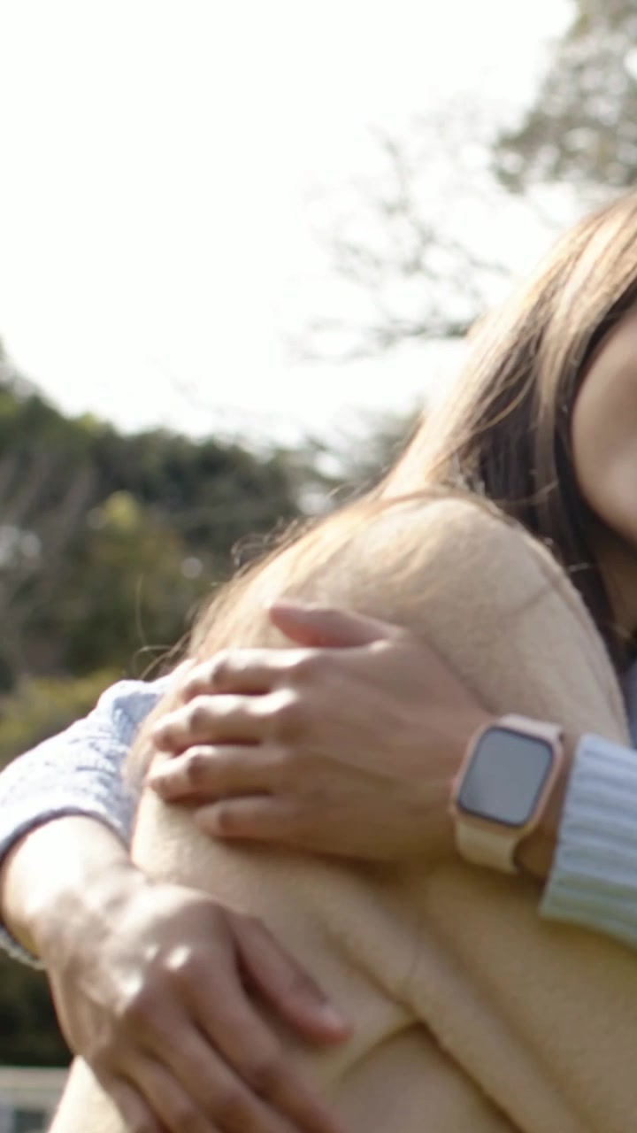 Video vertical: Mujeres sonriendo abrazándose en un parque por consuelo, vistiendo suéteres de punto con reloj inteligente.
