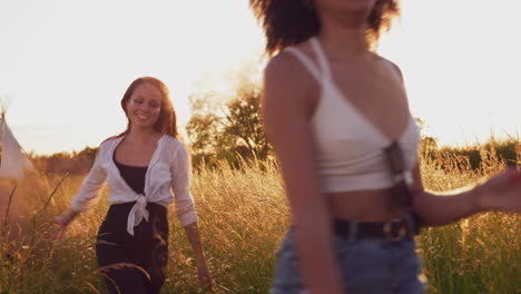 two female friends camping at music festival running through field with smoke flares